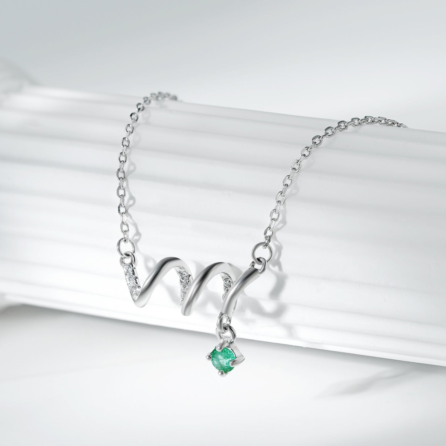 Silver necklace with a green gemstone pendant on a white background