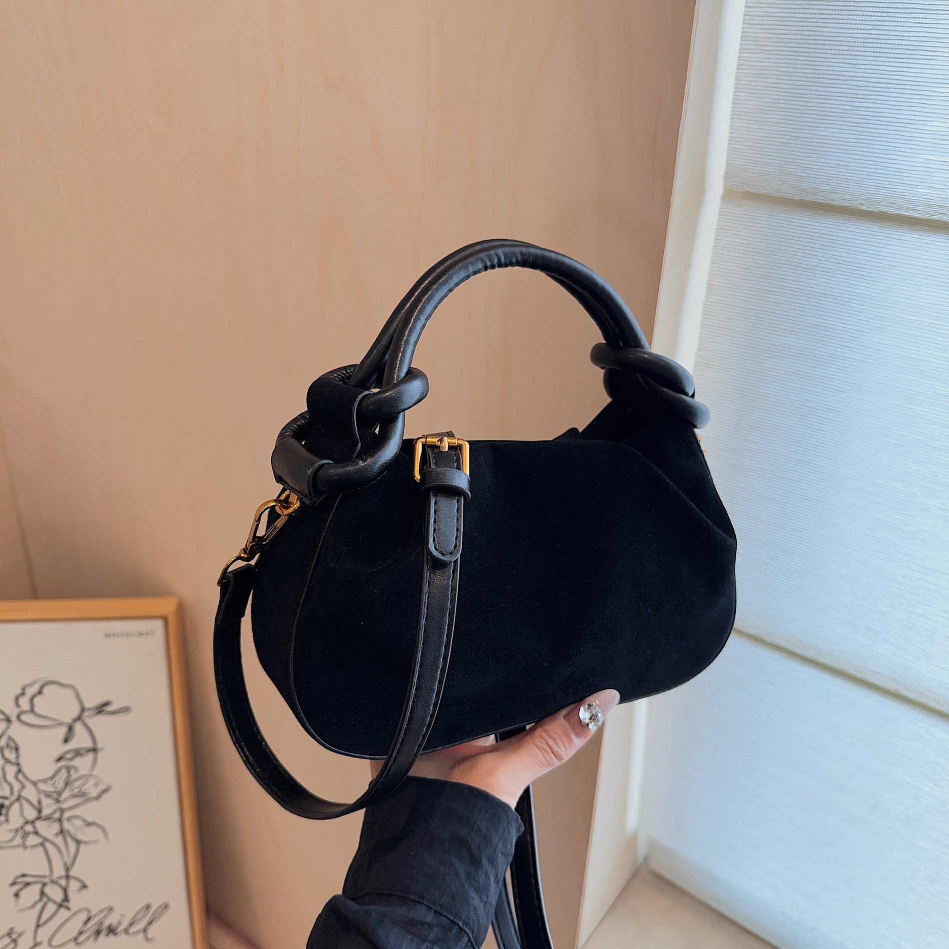 Black handbag held by a person against a neutral wall.