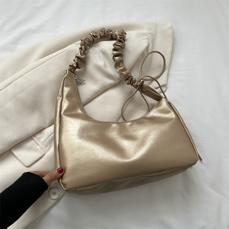 Beige handbag with ruched handle on a white surface