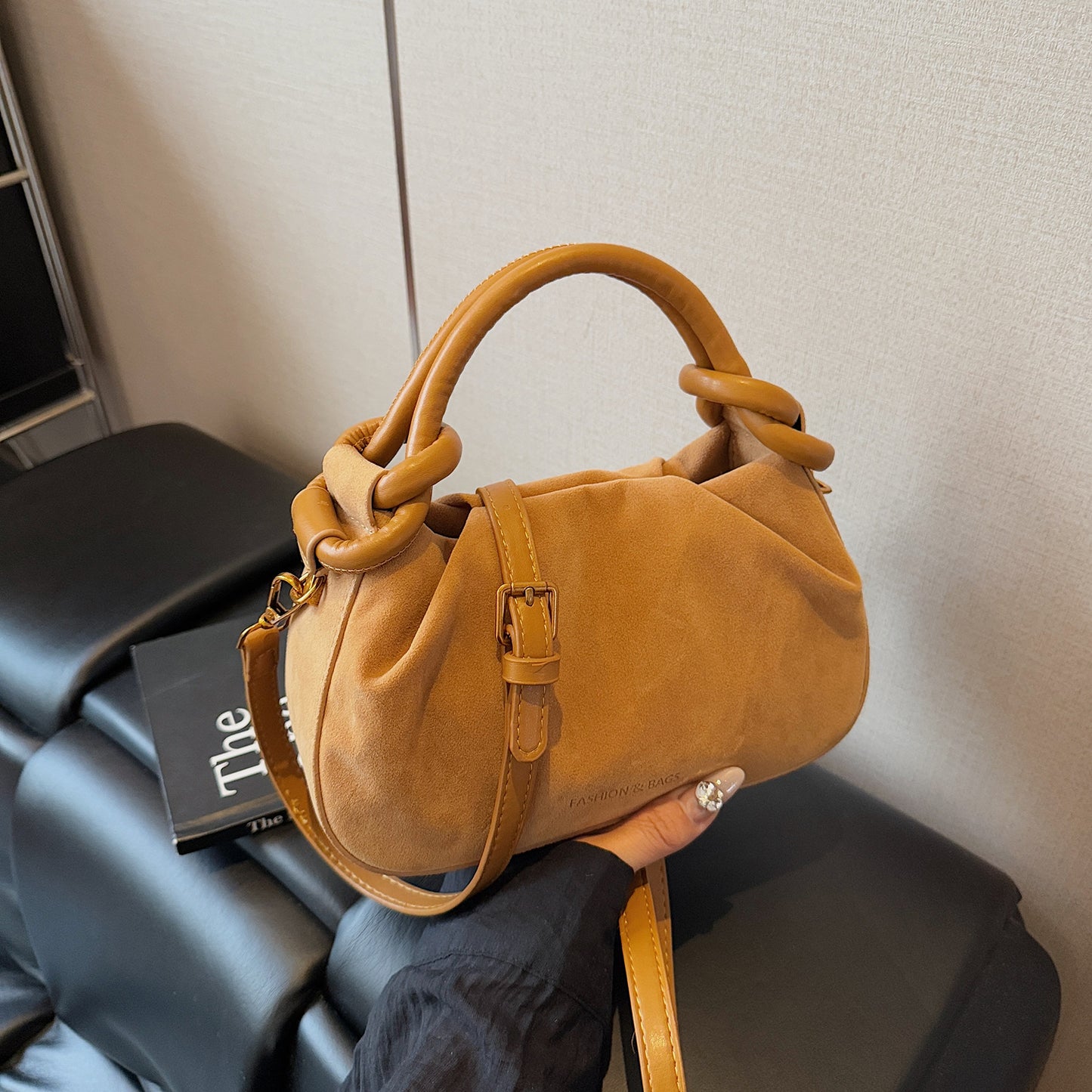 Brown handbag held by a person on a chair with a neutral background