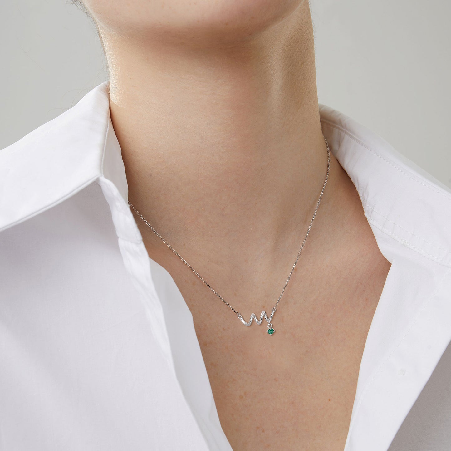 Silver necklace with a green gemstone on a person wearing a white shirt.