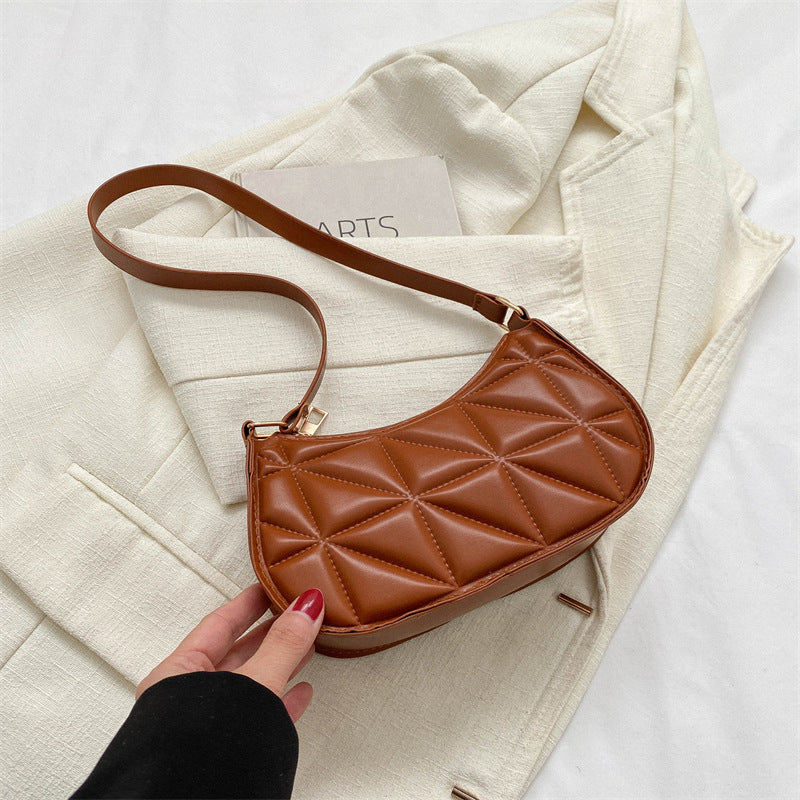 Brown quilted handbag held by a hand on a light background